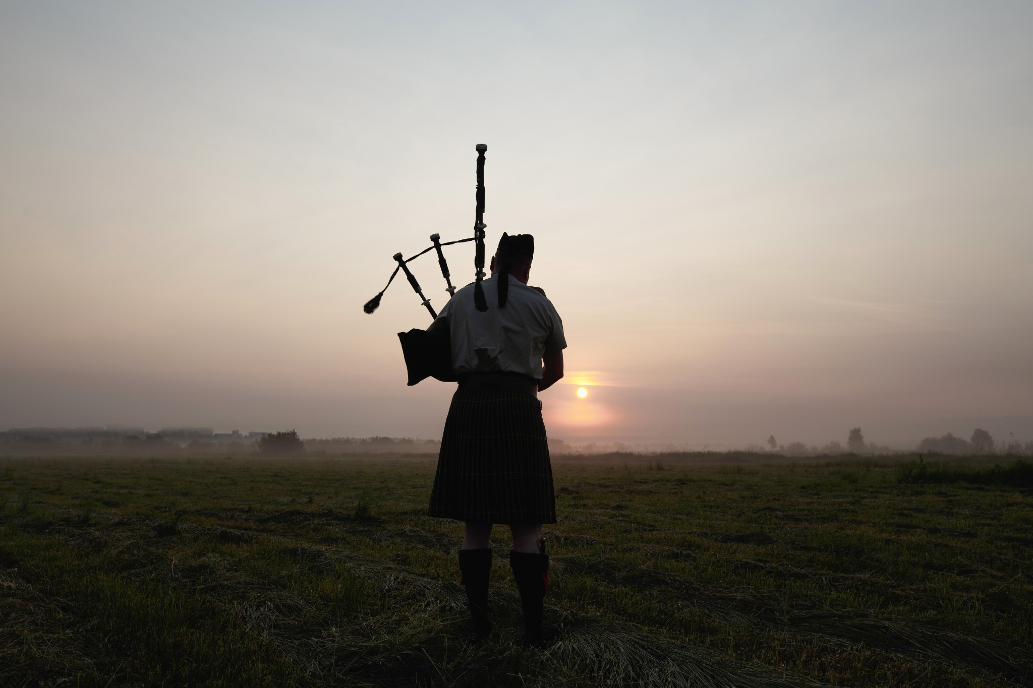 A man playing a bagpipe during a Scottish sunset.