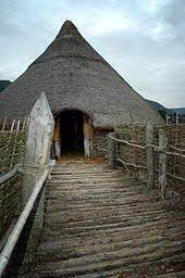 A wooden walkway leading to a straw crannog hut.