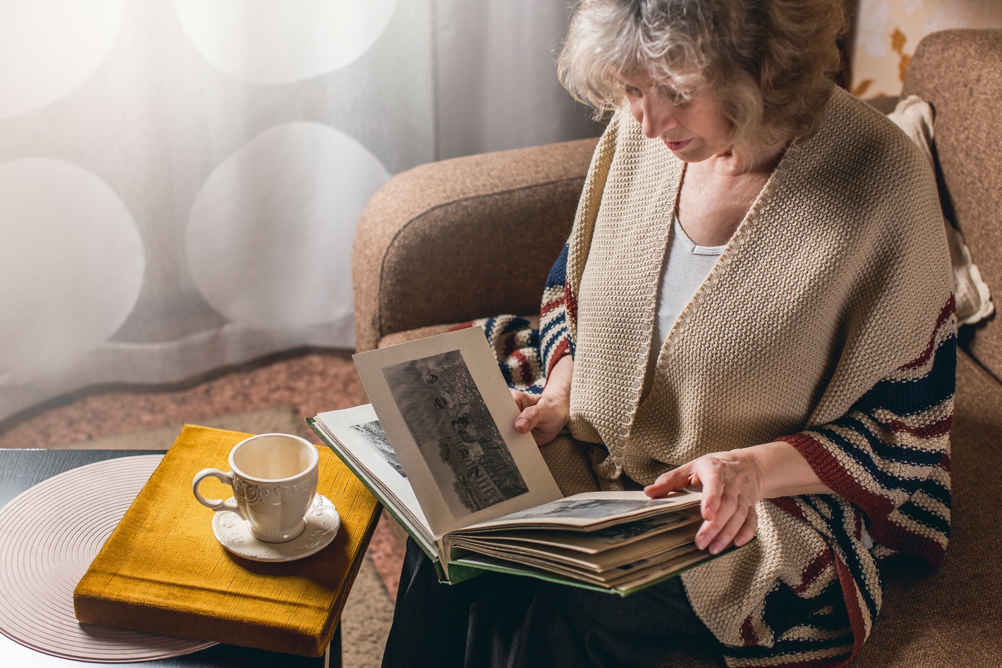 A elderly woman experiencing Hiraeth (the Welsh word for nostalgia) while looking at a photo album and having tea.