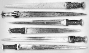 A row of Scottish dirks displayed on a white surface. A row of Scottish dirks displayed on a white surface.