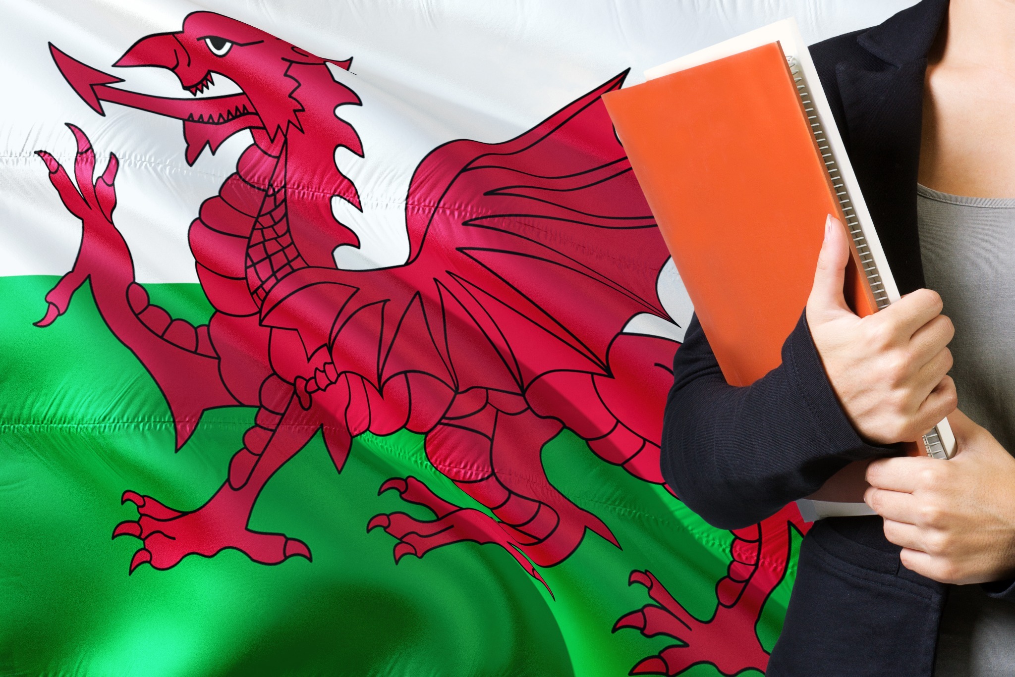 A woman holding a large notebook in front of a large Welsh flag