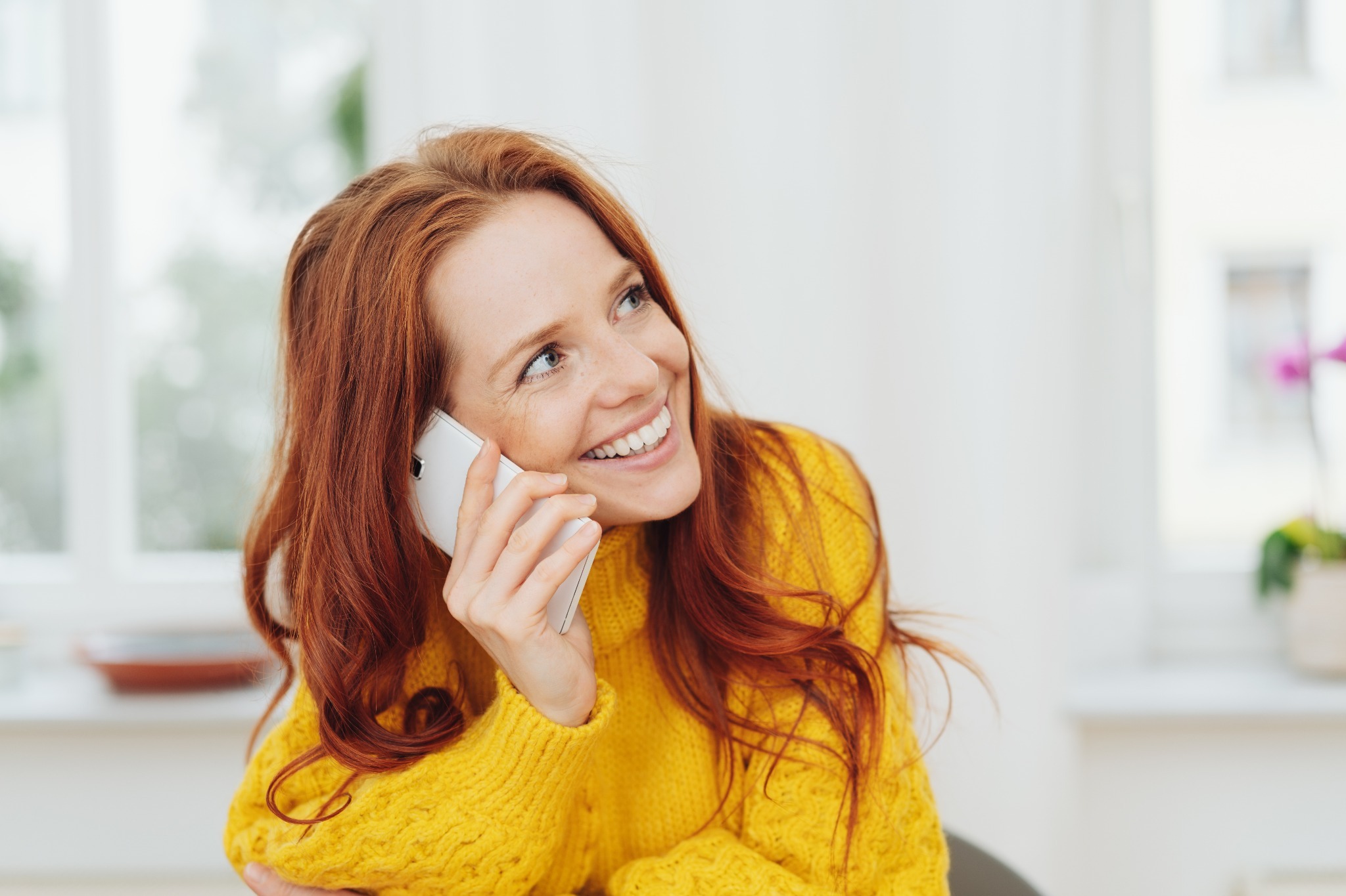 A red-headed woman talking on the phone and smiling, asking how someone is, or the Welsh phrase 