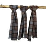 Three Tartan Scarf - OUTLANDER Premium Wool in brown, blue, and maroon tones are draped over a wooden branch, each knotted at the top.