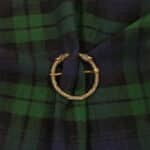 A Raven Penannular Brooch with intertwined snake heads is used to hold together a piece of dark green and navy blue tartan fabric, evoking the mystique of a raven's midnight flight.