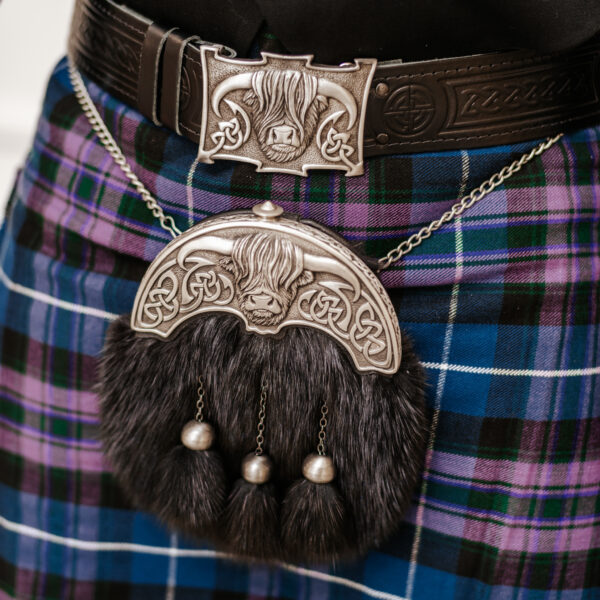 Close-up of a person wearing a traditional Scottish kilt with a detailed sporran and the Celtic Embossed Quality Leather Kilt Belt. The sporran features a hairy motif with three metallic tassels, and the belt flaunts an intricate embossed design.