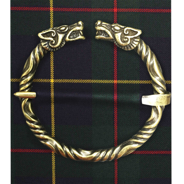 A Wolf Penannular Brooch featuring two wolf heads is placed on a background with a red, green, and yellow plaid pattern.