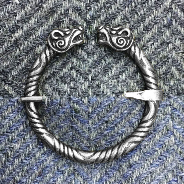 A Bear Penannular Brooch featuring dragon head designs on both ends, pinned on a herringbone-patterned fabric background.