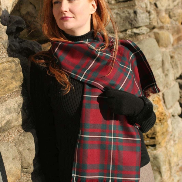 A woman with red hair is leaning against a stone wall, dressed in an Old & Rare Premium Wool Tartan Scarves Set of 2.