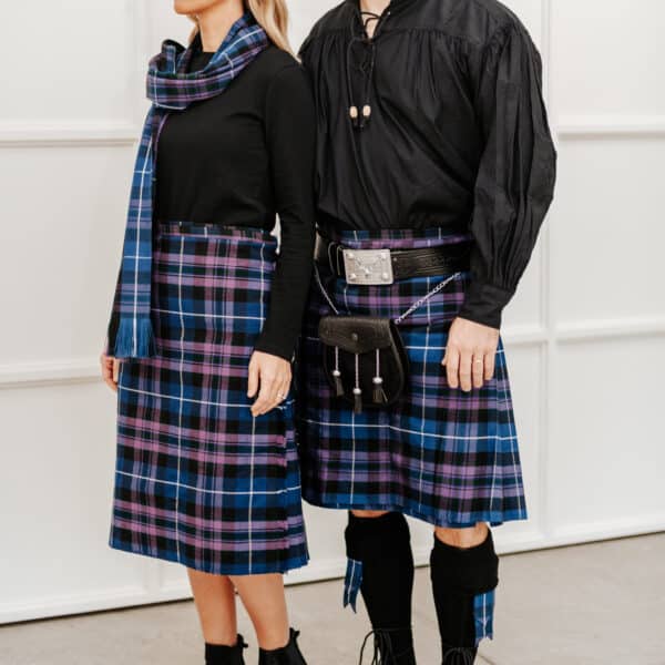 Two people are dressed in traditional Scottish attire with matching tartan patterns, including a kilt and scarf, both paired with a Rustic Highland Lace-Up Kilt Shirt.