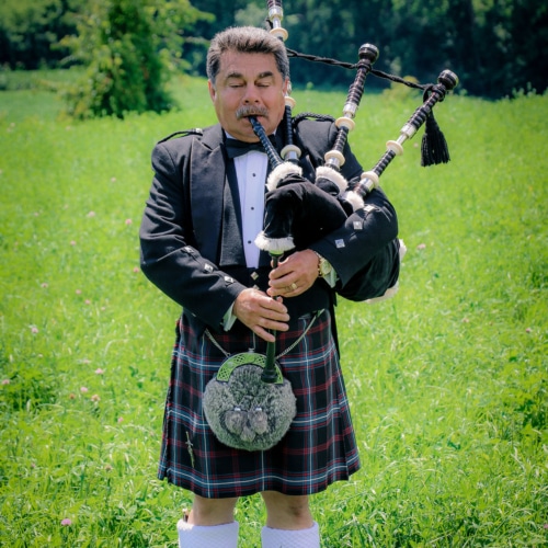 Welcome to Celtic Croft! Imagine a mesmerizing scene in a field where a man, adorned in traditional attire, passionately plays the bagpipes. His kilt gracefully sways with each powerful note,