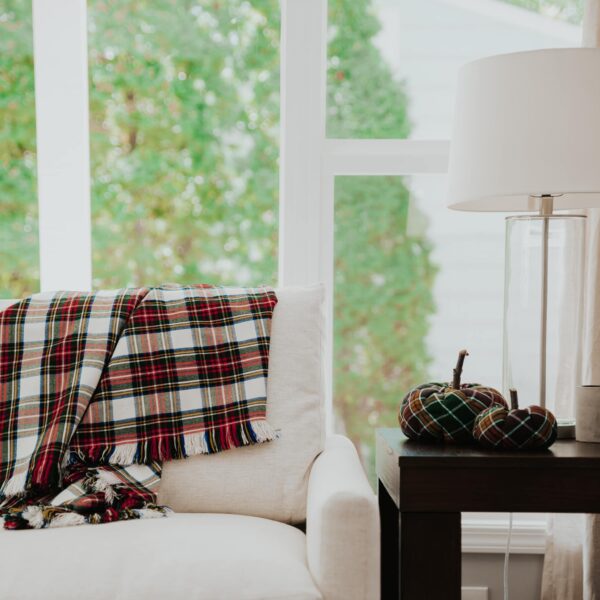 A Stewart Dress Homespun Tartan Blanket/Throw - 2 Yards sits on a chair in front of a window.