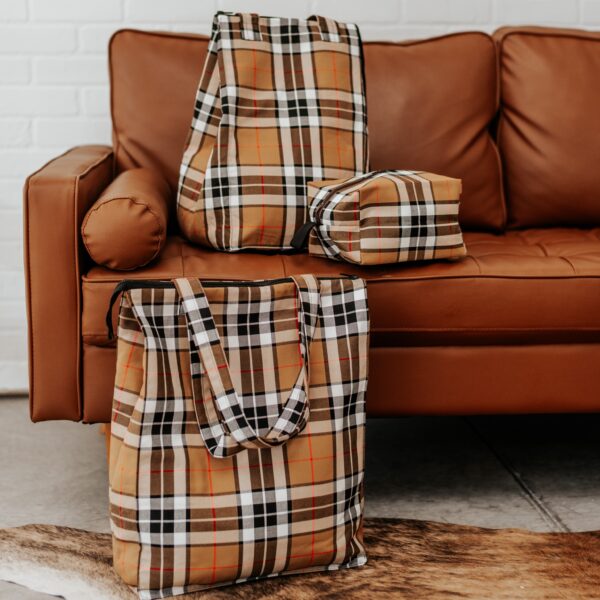 Three Thompson Camel Modern Tartan travel bags sitting on a leather couch.