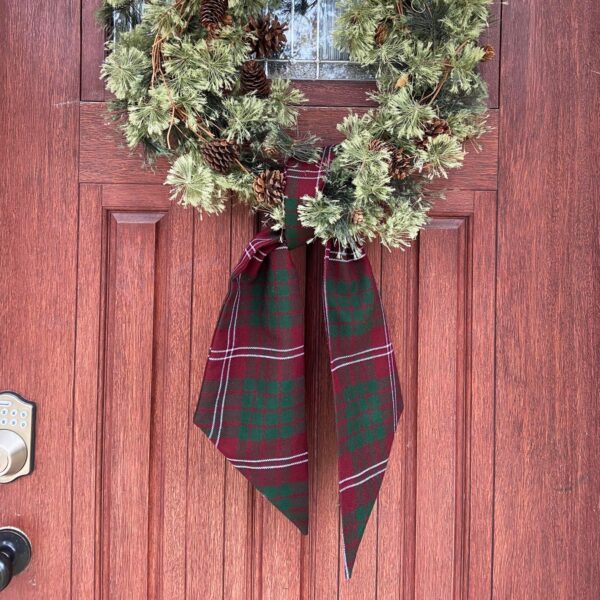 A Tartan Wreath Sash - Homespun Wool Blend hangs on a red door.