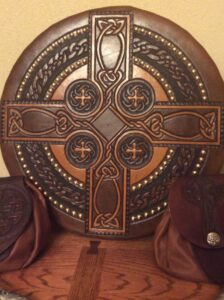 A wooden celtic cross adorned with leather pouches, providing the perfect Scottish Targe accessory.