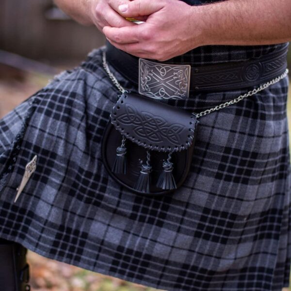 A man wearing a plaid kilt with tassels and a Saltire Antiqued Kilt Belt Buckle-sold 10/23.