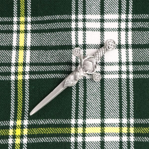 A green and yellow plaid cloth with a Stag's Head Kilt Pin on it.