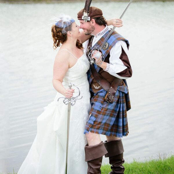 A bride and groom in Welsh Tartan Medium Weight Premium Wool Great Kilts kissing near a body of water.