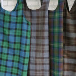 Four Tartan Cross Back Aprons - Homespun Wool Blend hanging on a rack.