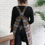 A woman wearing a Tartan Cross Back Apron - Homespun Wool Blend.