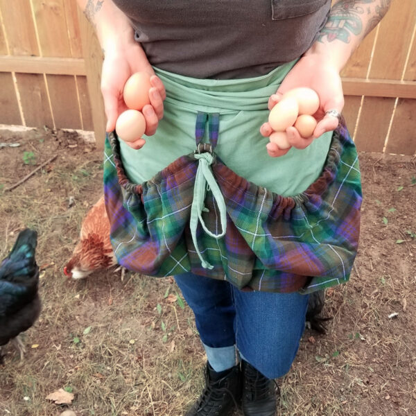 A woman holding eggs in a plaid Tartan Gathering Apron - Homespun Wool-Blend.