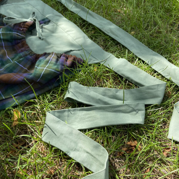 A Tartan Gathering Apron - Homespun Wool-Blend lying on the grass.