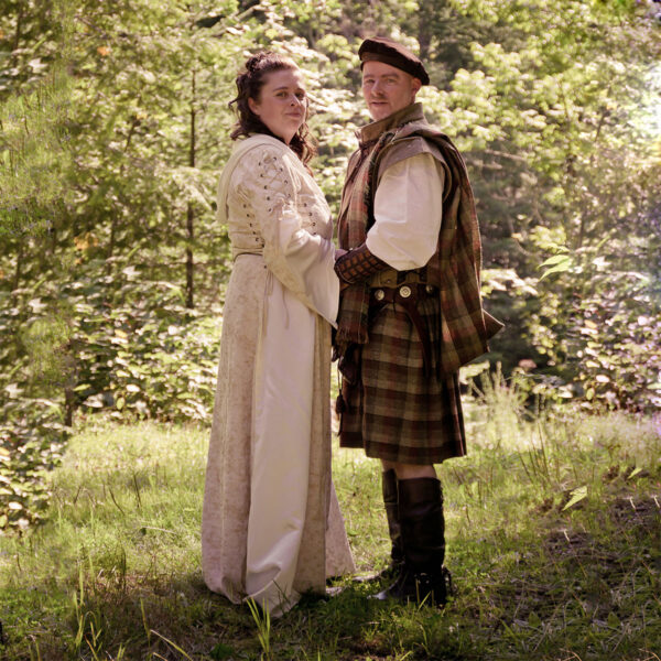 A man and woman in traditional clothing standing in a forest, wearing the Heavy Weight 16oz Premium Wool Ancient Kilts.