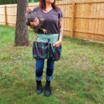 A woman holding a chicken in a Tartan Gathering Apron - Homespun Wool-Blend.