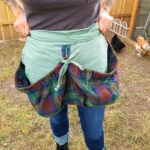 A woman wearing a green Tartan Gathering Apron - Homespun Wool-Blend.