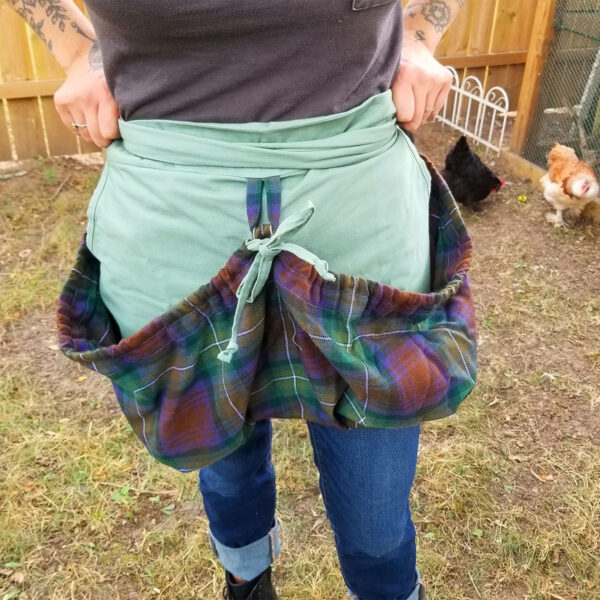 A woman wearing a green Tartan Gathering Apron - Homespun Wool-Blend.