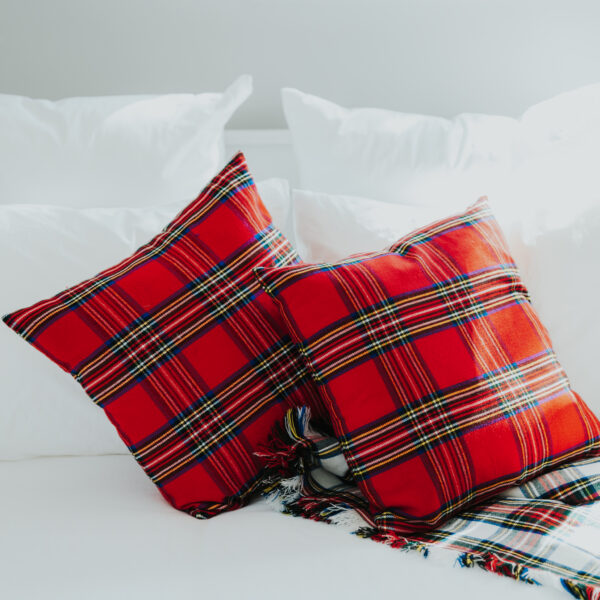 Two plaid pillows on a white bed adorned with a Homespun Tartan Blanket/Throw.