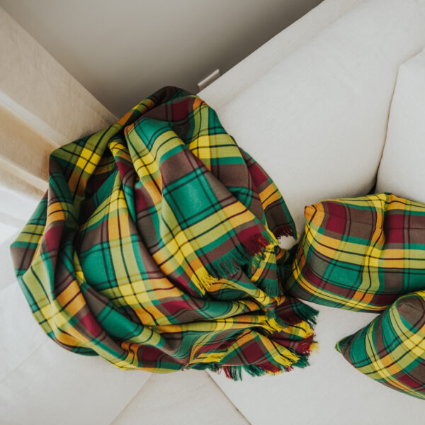 A green and yellow Homespun Tartan blanket on a white couch.