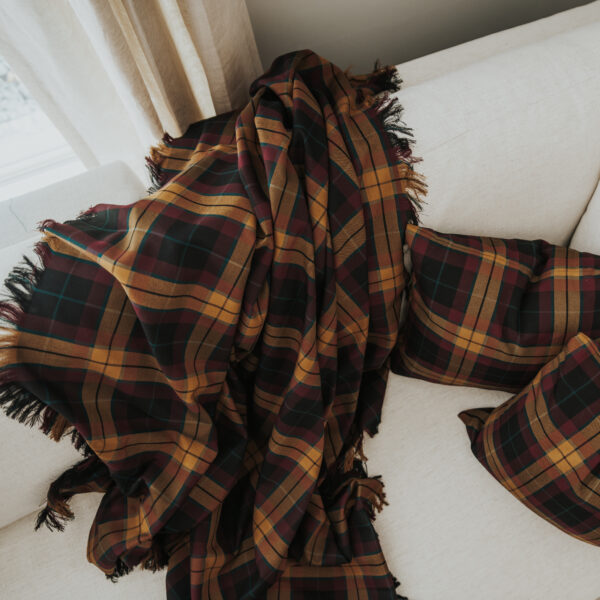 A Homespun Tartan Blanket/Throw on a cozy couch in front of a window.