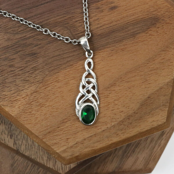 An Amethyst Celtic Knot necklace featuring an emerald pendant is delicately placed on a wooden table.