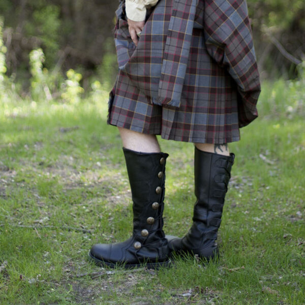 A woman in a plaid kilt standing in the grass, wearing Black Premium Leather Knee-High Boots.