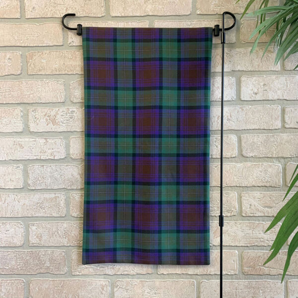 A Tartan Garden Flag - Homespun Wool Blend, purple and green in design, hanging on a brick wall.