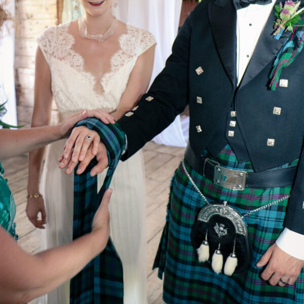 A man in a kilt and a woman in a white dress, celebrating their OUTLANDER Handfasting - Poly Viscose Tartan-inspired handfasting ceremony.