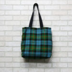 A Homespun Wool Blend Tartan Tote Bag hanging on a brick wall.