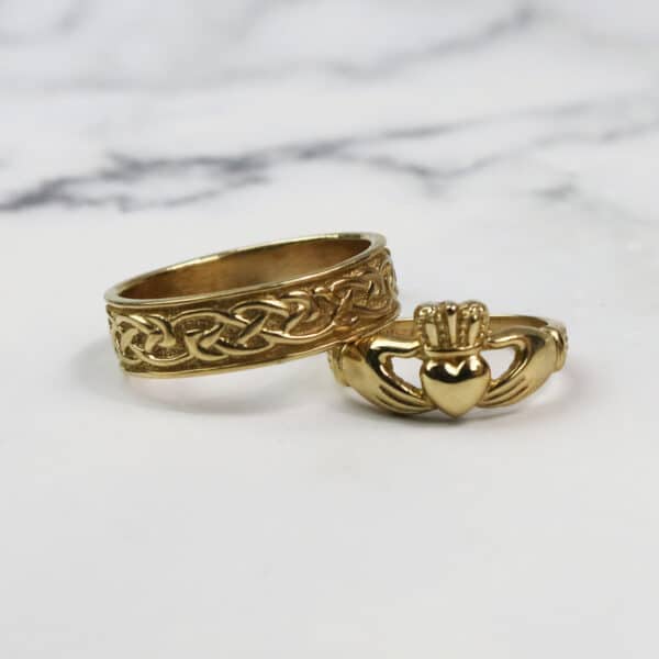 Two gold claddagh rings on a marble table.