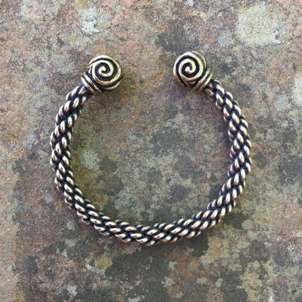 The Celtic Triskelion Torc Bracelet delicately placed on a stone surface.