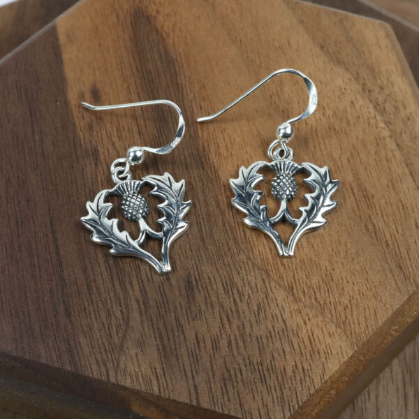 A pair of earrings on a wood surface, along with a Scottish Thistle Necklace.