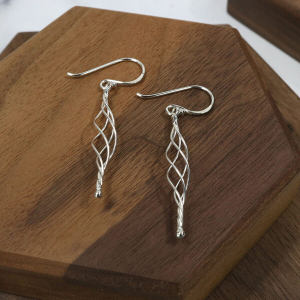 A pair of Triquetra Sterling Silver Earrings on a wooden table.