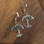 A stunning pair of Tree of Life Earrings resting elegantly on a rustic wooden table.