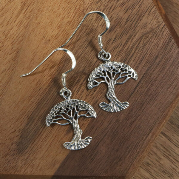 A stunning pair of Tree of Life Earrings resting elegantly on a rustic wooden table.