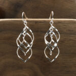A pair of Triquetra Sterling Silver Earrings on a wooden surface.