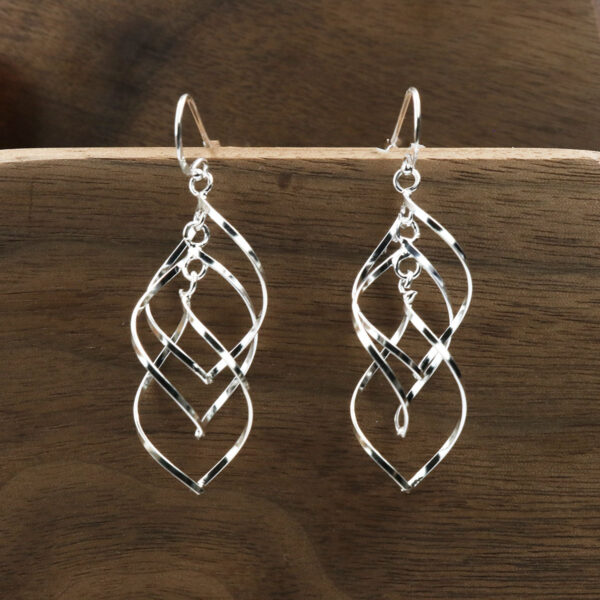 A pair of Triquetra Sterling Silver Earrings on a wooden surface.