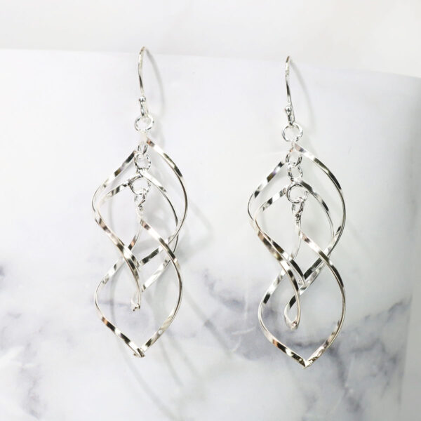 A pair of Triquetra Sterling Silver Earrings on a marble table.