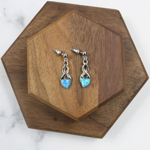 A pair of blue opal Triquetra Sterling Silver earrings on a wooden board.
