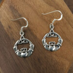 A pair of Sterling Silver Triquetra Claddagh Earrings on a wooden table.