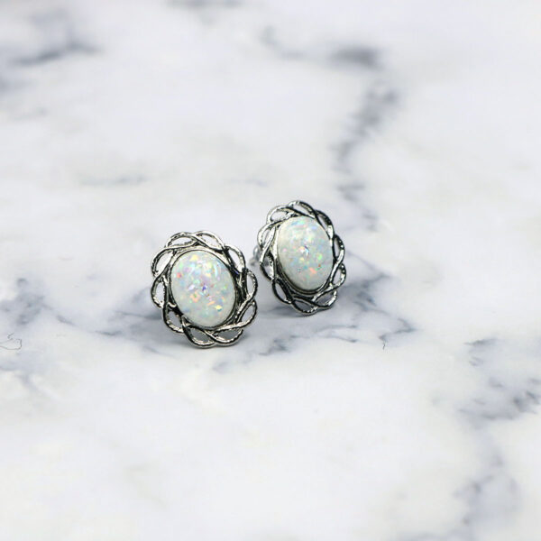A pair of white Opal Knot stud earrings on a marble surface.