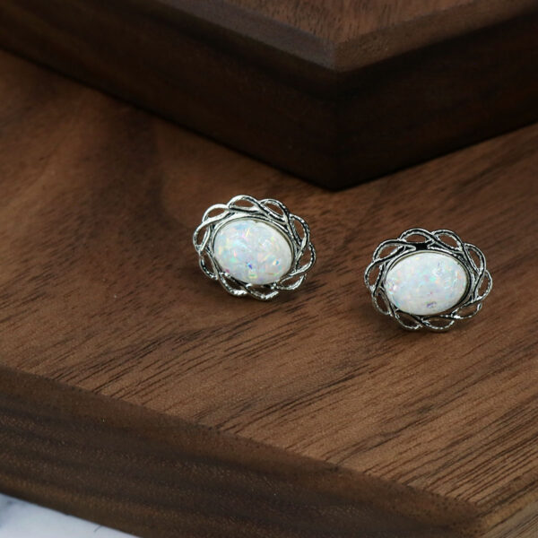 A pair of Opal Knot Stud Earrings showcasing stunning white opals, resting elegantly on a wooden table.